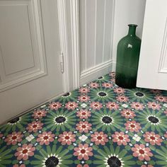 a green vase sitting on the floor in front of a white wall and door way