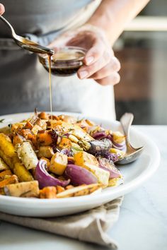 a person is pouring sauce over a plate of food that includes potatoes, onions and carrots