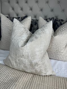 three pillows on top of a bed with white sheets and grey headboard in the background