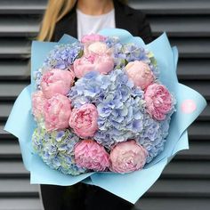 a woman holding a bouquet of pink and blue flowers in front of a gray wall