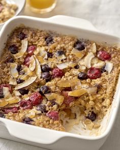 baked oatmeal with fruit and nuts in a white dish next to a glass of orange juice