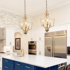 a kitchen with white cabinets and blue island in the center, two pendant lights hanging from the ceiling