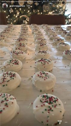 white frosted cookies with sprinkles on a table in front of a christmas tree