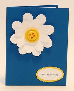 a blue card with a white flower and a yellow button on the front that says you're invited