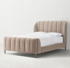 an upholstered bed with white linens and wooden legs in a minimal bedroom