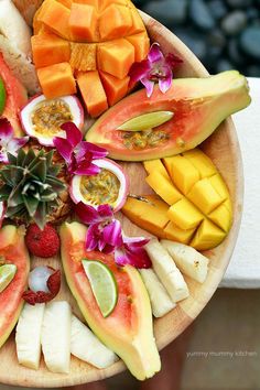 a wooden plate topped with sliced fruit and veggies on top of a table