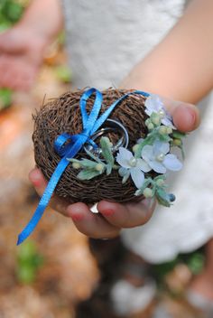 a person holding a bird's nest with flowers on it and a blue ribbon