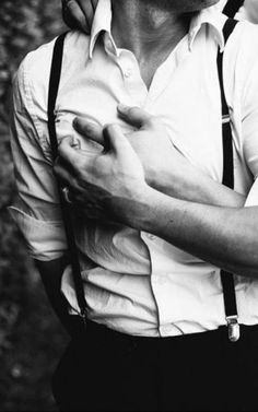 a man in suspenders is holding his hand on his chest