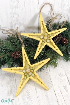 two yellow star ornaments hanging from a pine branch on a white wooden background with pine cones and twine of twine