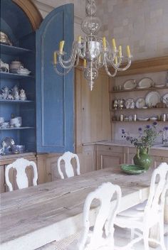 a dining room table with white chairs next to a blue cabinet and china cabinet in the background