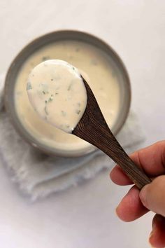 a hand holding a wooden spoon over a bowl of yogurt with a cloth napkin on the side