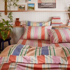 a bed with colorful sheets and pillows in a room filled with potted plants on the wall