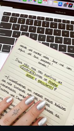 a woman's hand holding a notebook in front of a laptop computer with writing on it