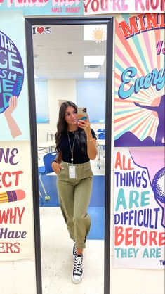 a woman taking a selfie in front of a mirror with posters behind her on the wall