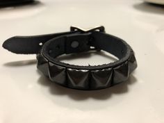 "Handmade black leather punk bracelet with one row of pyramid studs. Great for layering with other bracelets and chains. This is my bestselling studded leather bracelet. Has an adjustable strap and buckle closure so it's harder to lose. Made with thick, hand dyed vegetable tan leather. This is real cowhide, not cheap bonded leather that's going to fall apart eventually. Nickle plated steel studs and hardware. Studs are all set by hand. Small sizes have fewer than 9 studs. Also available with bla Punk Black Bracelet With Silver Studs, Rock Style Leather Bracelet With Studs For Festivals, Rock Style Studded Leather Bracelet For Festivals, Edgy Adjustable Bracelets With Studs, Adjustable Punk Leather Bracelet With Studs, Adjustable Studded Leather Punk Bracelet, Adjustable Studded Leather Bracelet In Punk Style, Adjustable Spiked Leather Bracelet For Festivals, Adjustable Rock Style Bracelet With Studs