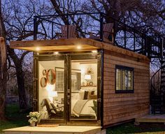 a small wooden cabin sitting in the middle of a forest at night with its lights on