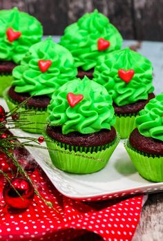 cupcakes decorated with green frosting and red hearts on a white platter