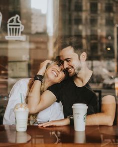 a man and woman sitting at a table in front of a window with coffee cups