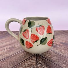 a ceramic mug with strawberries on it sitting on top of a wooden table next to a pink wall