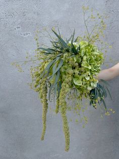 a person holding a bouquet of green flowers and greenery against a gray concrete wall