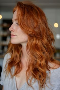 Woman with long, wavy red hair and freckles, looking to the side, in a softly lit indoor setting.