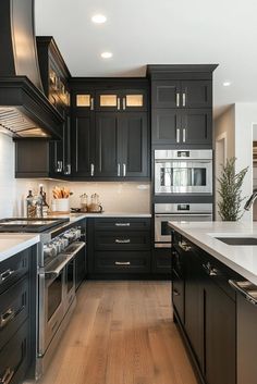 a large kitchen with black cabinets and white counter tops, stainless steel appliances and wooden floors