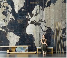 a woman is sitting on a bench in front of a wall with a world map