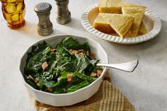 a white bowl filled with spinach next to two slices of bread on top of a table