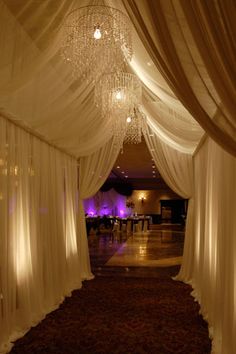 a long hallway with white drapes and chandelier hanging from the ceiling