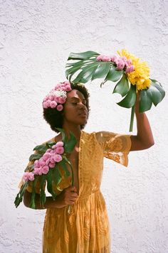 a woman with flowers in her hair holding a large leaf and flower arrangement on her head