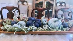 a wooden tray filled with blue pumpkins and greenery on top of a table