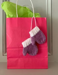 a pair of knitted mittens sitting on top of a pink shopping bag