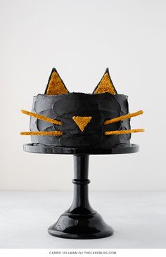 a black cake decorated with gold glitters and a cat's head on top