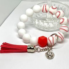 a red and white beaded bracelet with a baseball charm on it, sitting next to a glass bowl