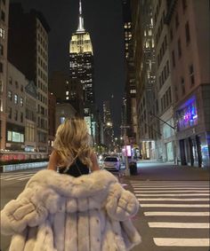 a woman is walking down the street at night with her fur coat over her shoulders