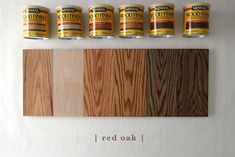 five cans of red oak sitting on top of a white wall next to some wood planks