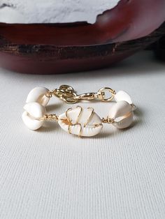 A sultry bracelet with the prettiest cowries. Center cowry is wire wrapped for interest. Done in your choice of gold or silver plated wire. Bold toggle clasp, XL ivory shells, and thick jumprings for extenders make this bracelet stand out. Fits from a 6.5" to 8.5" wrist.  Comes boxed and ready for gifting. Adjustable Cowrie Shell Bracelet Jewelry, Adjustable Cowrie Shell Bracelet, Artisan Adjustable Cowrie Shell Jewelry, Artisan Cowrie Shell Jewelry, White Cowrie Shell Bracelet, Artisan Beach Bracelet, Beach Gold Hand Wrapped Jewelry, Gold Hand Wrapped Jewelry For The Beach, Artisan Shell Jewelry With Adjustable Fit