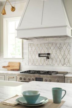 a white kitchen with an oven, stove and two cups on the counter top in front of it