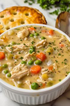 a bowl of chicken pot pie soup next to a piece of bread on a table