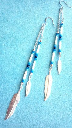 two white and blue beads are hanging from silver earwires on a blue background