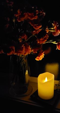 a lit candle sitting on top of a table next to a vase filled with flowers