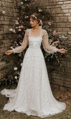 a woman standing in front of a brick wall wearing a wedding dress with long sleeves