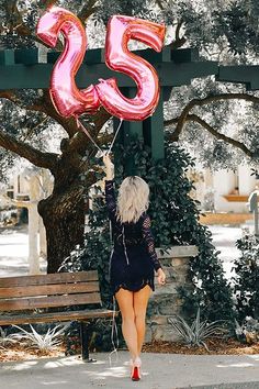 a woman walking down the street with a large pink number 25 balloon in her hand