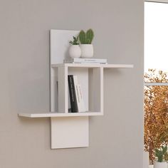 there is a white shelf with books on it next to a potted plant and window