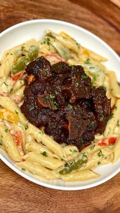 a white plate topped with pasta and meat covered in sauce on top of a wooden table