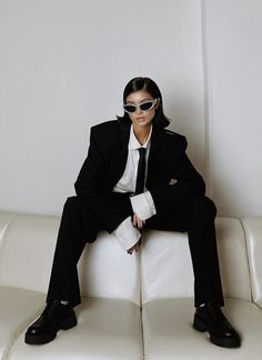 a man in a suit and sunglasses sitting on a white couch with his legs crossed