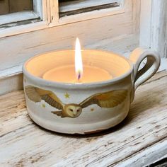 a candle that is sitting in a cup on a window sill with an owl painted on it