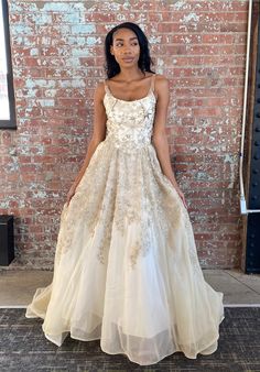 a woman standing in front of a brick wall wearing a white dress with gold sequins