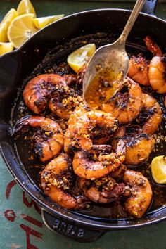 a skillet filled with cooked shrimp and lemon wedges on top of a table