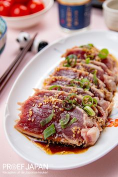 a white plate topped with meat covered in sauce and garnished with green onions